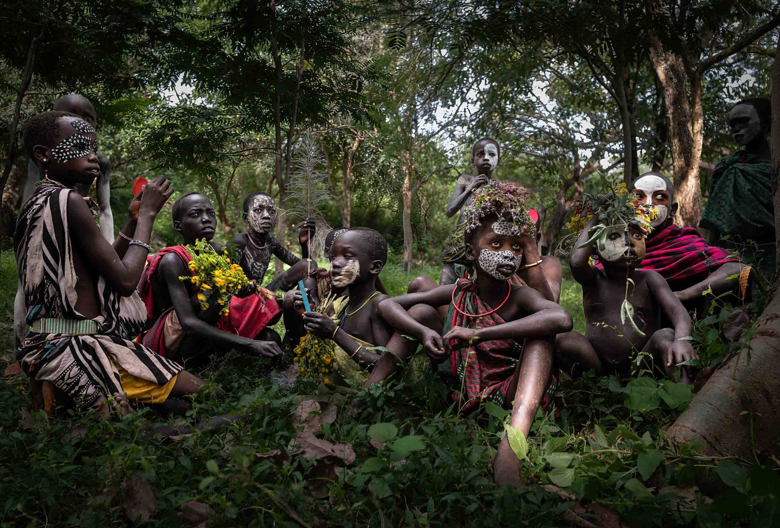 Suri men and children sitting in a forest clearing, Omo Valley, Ethiopia