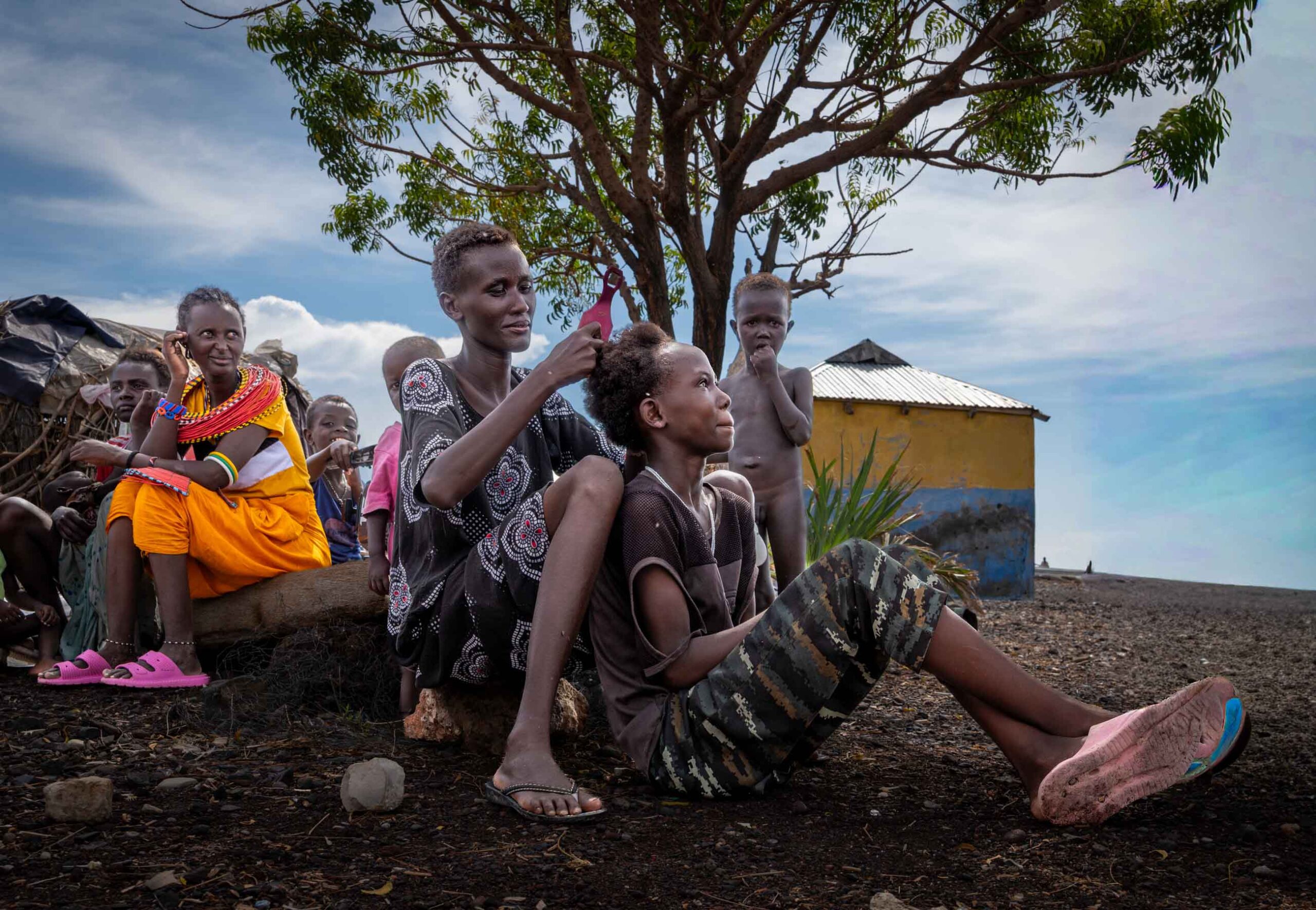 Two women braiding a girl's hair under a tree, northern Kenya