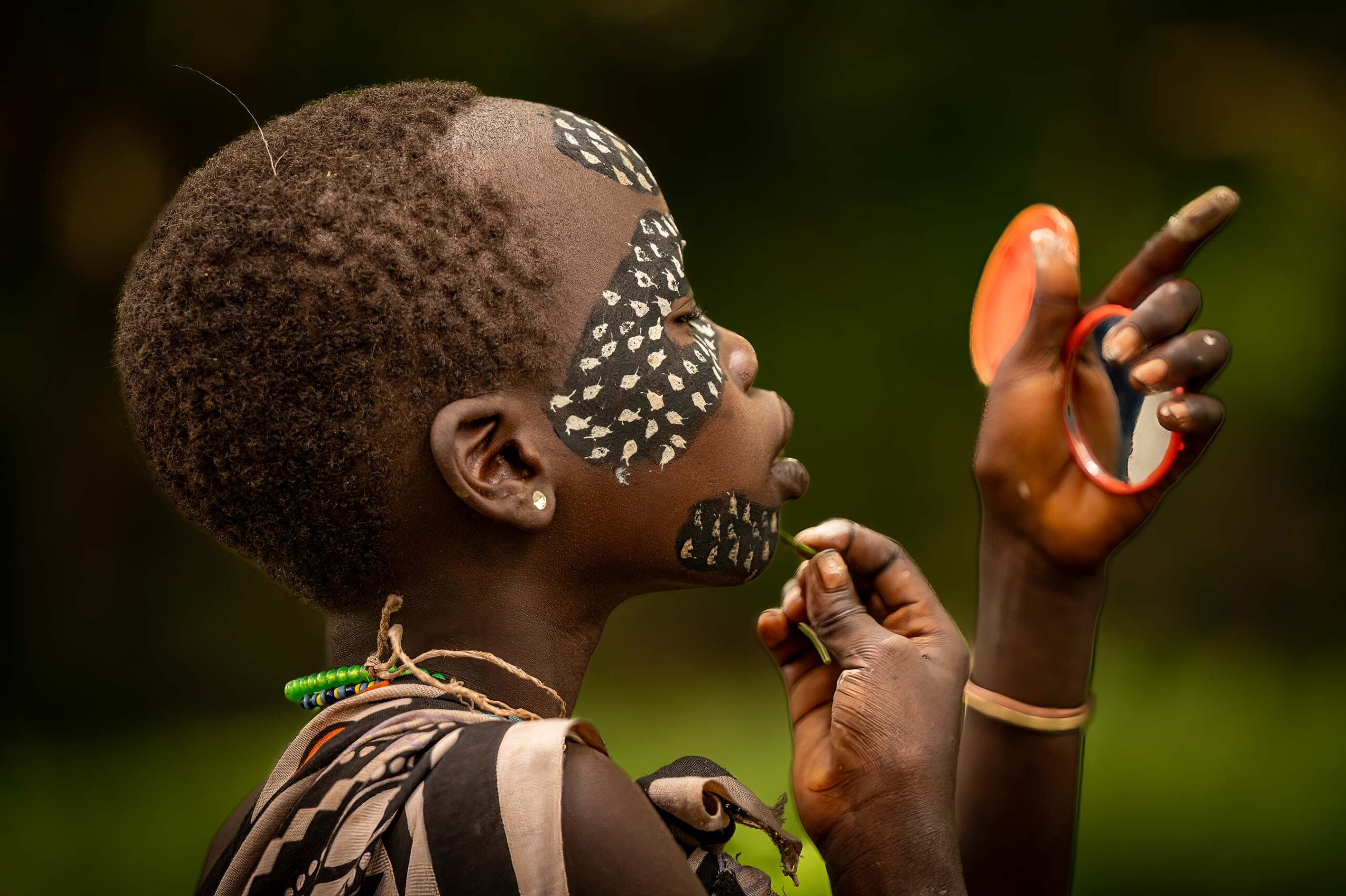 Girl with painted face holding a mirror, Omo Valley, Ethiopia