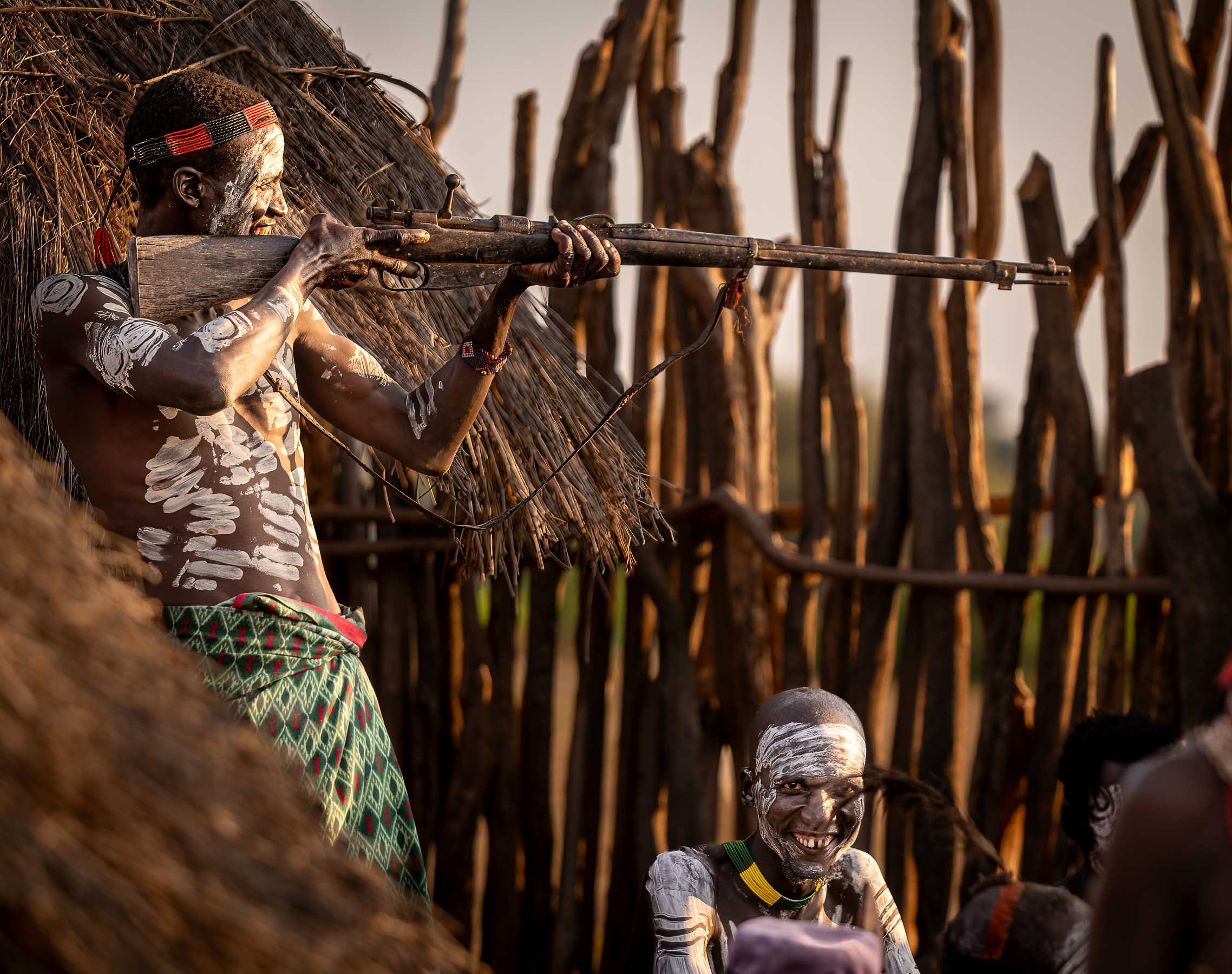 A man aiming a rifle beside a wooden fence, Omo Valley, Ethiopia