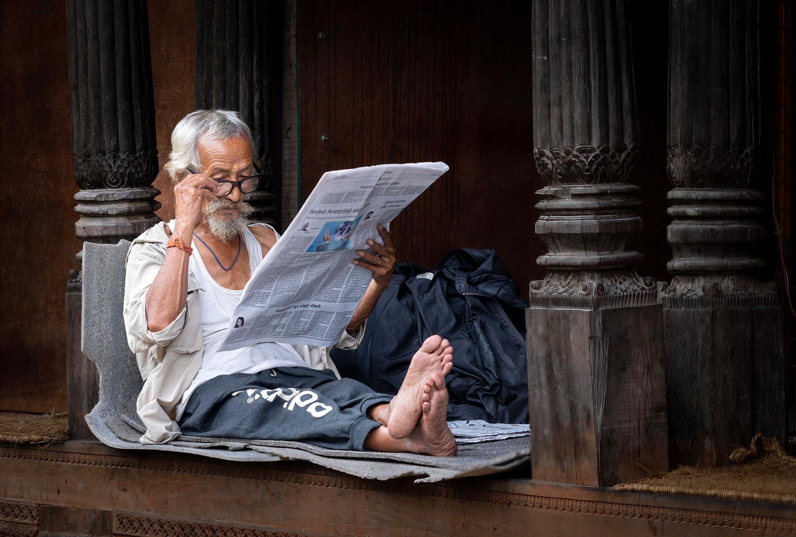 Man reading a newspaper on a temple platform, Nepal
