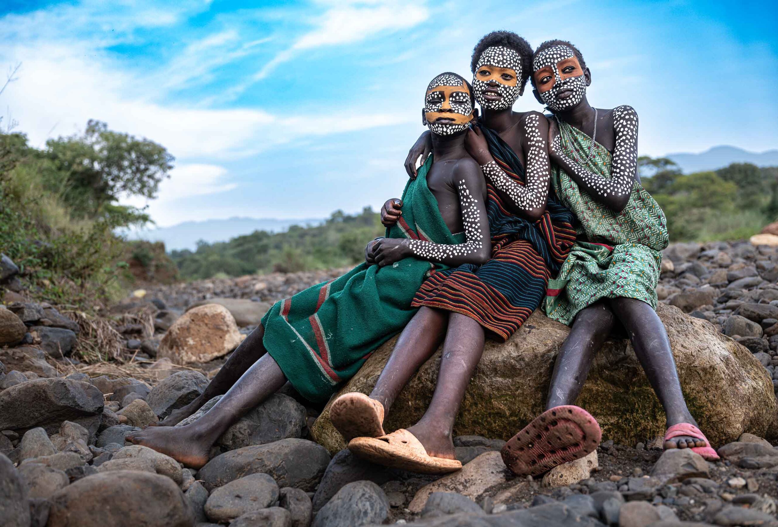 Three girls with painted faces sitting on a rock, Omo Valley, Ethiopia
