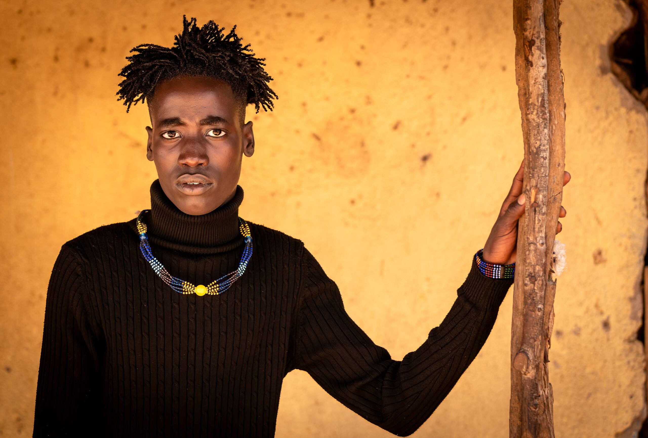 Young man standing against an orange wall, Omo Valley, Ethiopia